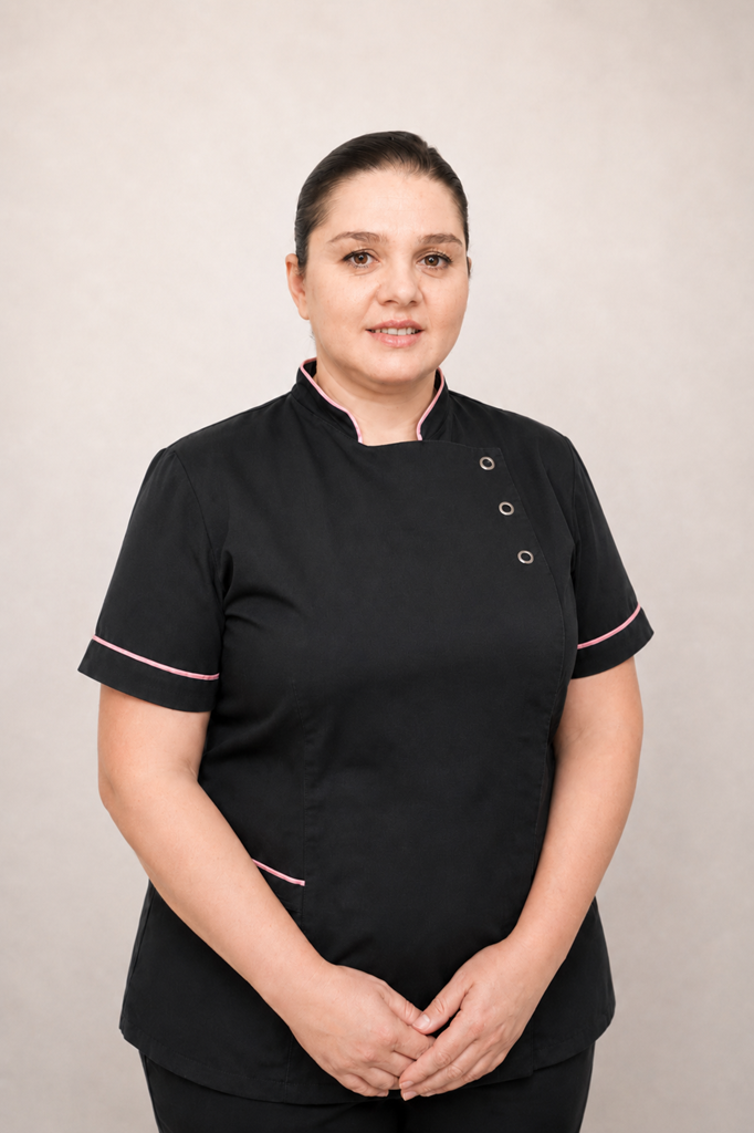 Portrait of a woman in a black medical uniform with pink trim, standing with hands folded in front.